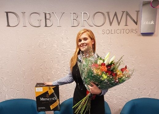 Jennifer Watson, Dundee Personal Injury Solicitor, with bouquet of flowers and case of prosecco from client