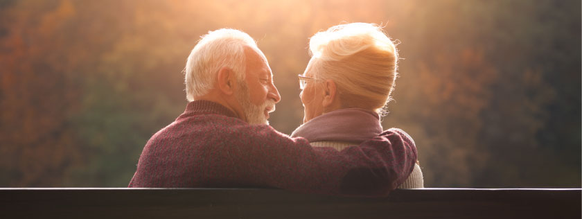 Older man and woman sitting on a bench talking and smiling