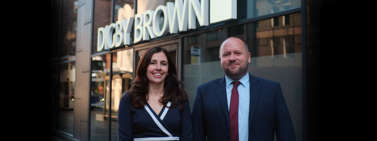 Hannah Bennett and Craig Smillie standing in front of the Digby Brown Glasgow office smiling