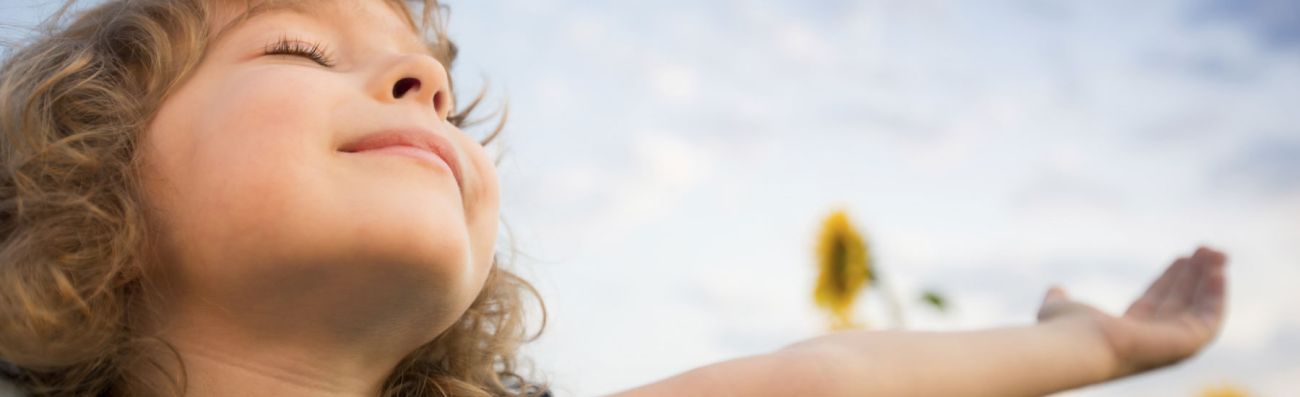 Child enjoying sunshine with eyes shut and arms wide