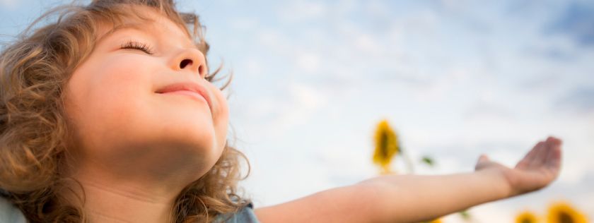 Child enjoying sunshine with eyes shut and arms wide