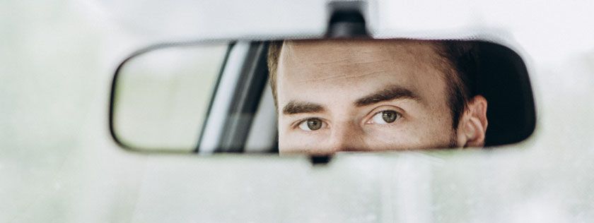 Man looking in rear view mirror in car