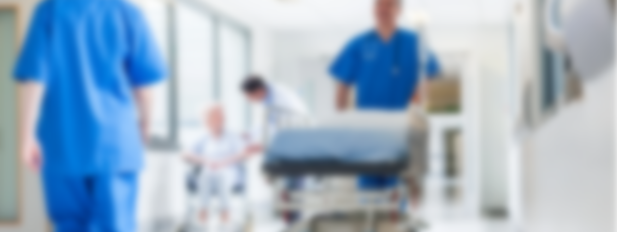 A hospital corridor with staff walking, one is pushing a hospital bed - the image is blurred.