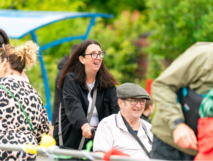 A woman smiling pushing a man in a wheelchair who is also smiling