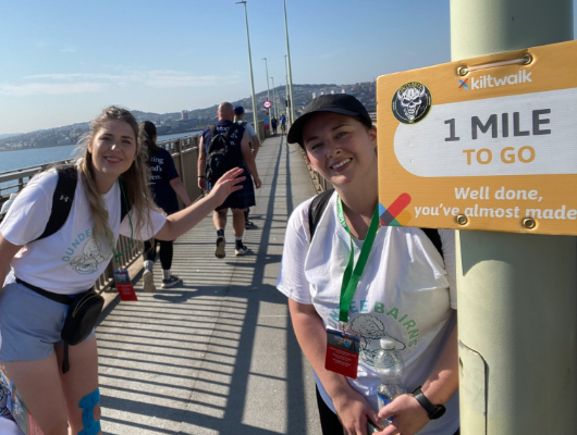 Dundee staff standing on the Tay Road Bridge next to a '1 mile to go' sign