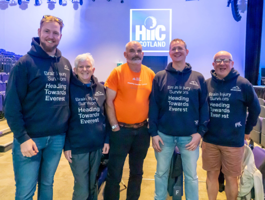 Image shows five individuals who completed a trek to Everest base camp. The group is made up of brain injury survivors and family members. They are wearing Heading to Everest branded hoodies.
