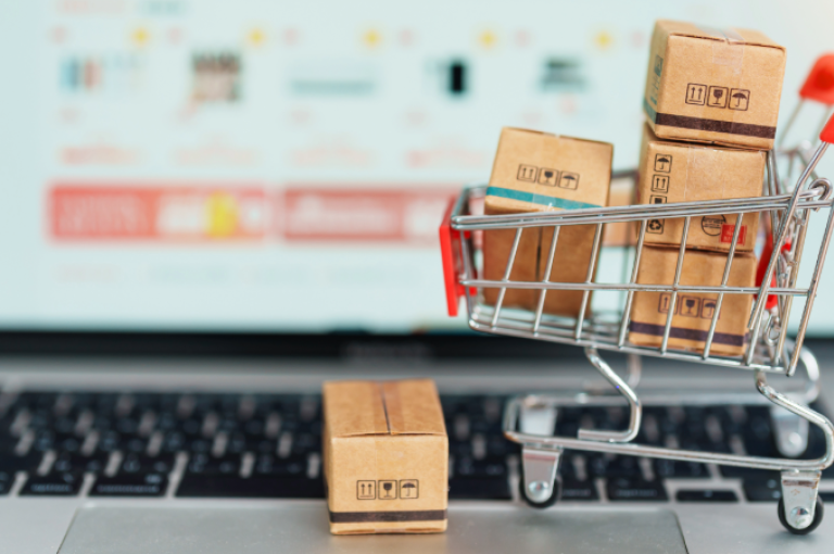 A laptop pictured on an online shopping page - blurred. A small shopping trolley sits on the keyboard filled with small boxes.