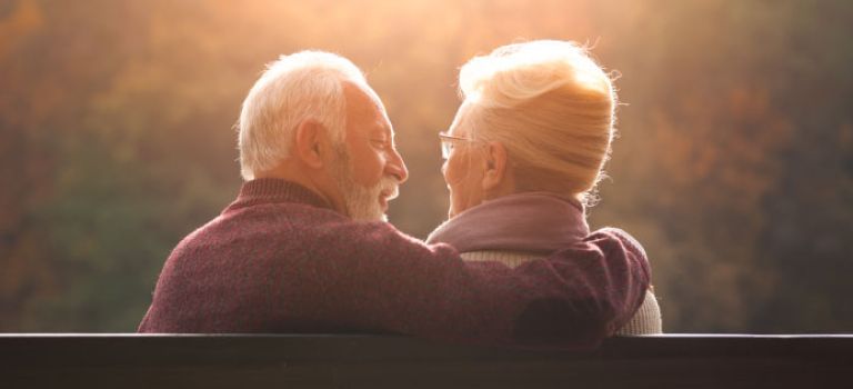 Older man and woman sitting on a bench talking and smiling