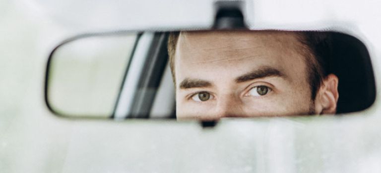 Man looking in rear view mirror in car