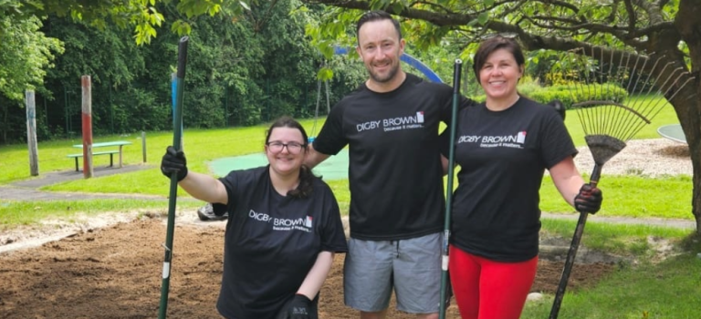 Three staff members from our Glasgow office standing in a garden with gardening tools