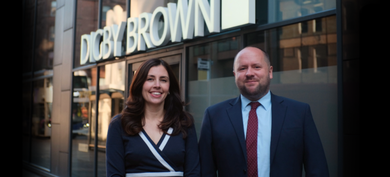 Hannah Bennett and Craig Smillie standing in front of the Digby Brown Glasgow office smiling