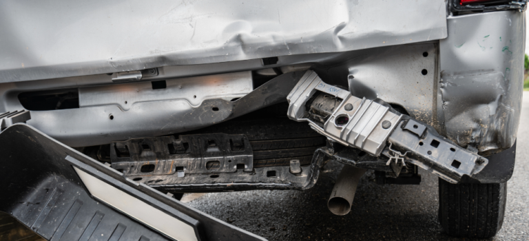 An image showing the back of a silver van which has been hit by a car. The back of the van is dented and the bumper has fallen off.