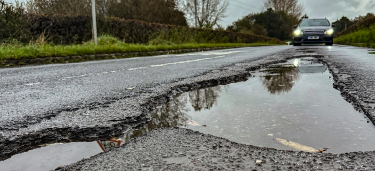 A large pothole on the road filled with water