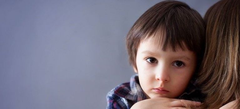 Unhappy child looking over mum's shoulder